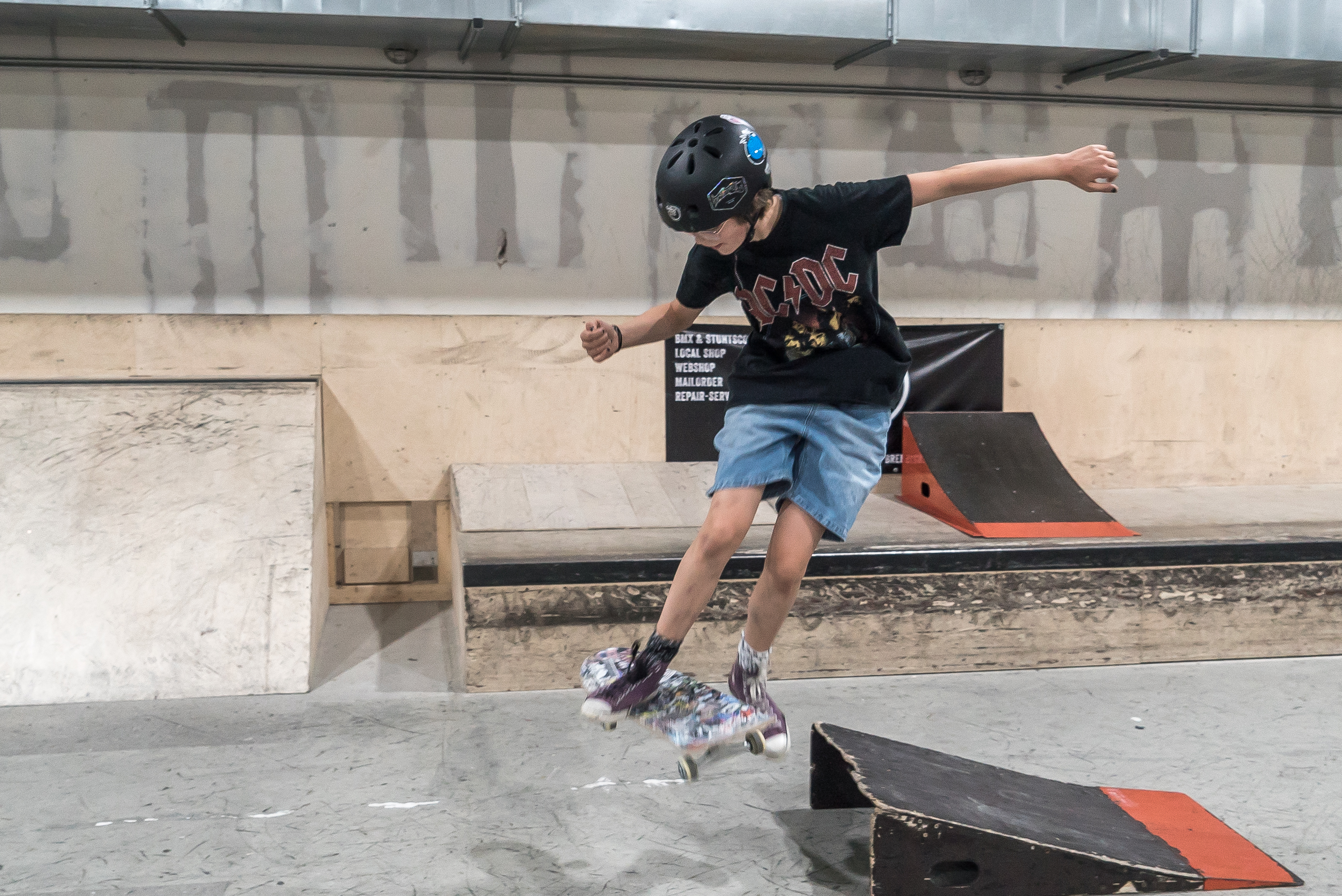Ein M&auml;dchen mit AC DC T-Shirt springt mit ihrem Skateboard &uuml;ber eine kleine Rampe.